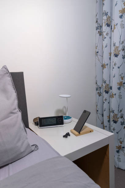 istock Smartphone on the bedside table with lamp, headset, clock and fragment of bed. Vertical view 1456612359