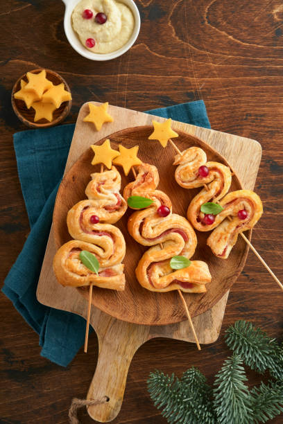 istock Christmas or New Year appetizer. Christmas tree shape puff pastry buns with cheese and ham. Group of Christmas tree shapes on wooden board. Festive idea for Christmas or New Year dinner. Top view. 1456612514