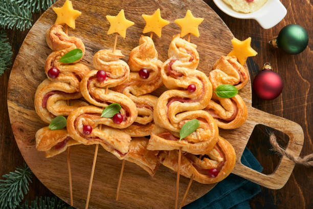 istock Christmas or New Year appetizer. Christmas tree shape puff pastry buns with cheese and ham. Group of Christmas tree shapes on wooden board. Festive idea for Christmas or New Year dinner. Top view. 1456612567