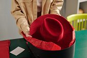 Young craftswoman putting new crimson felt panama hat into black round box