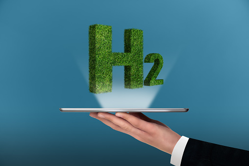 A man is holding a digital tablet with symbol of Hydrogen H2 from grass