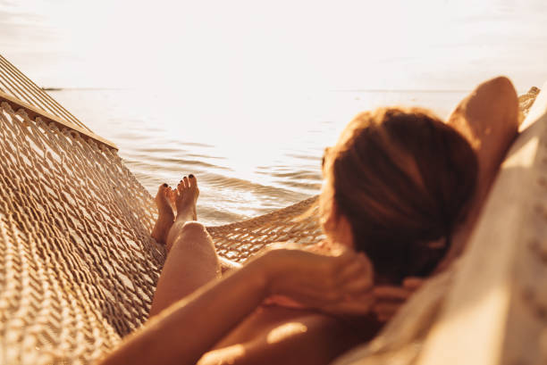 junge frau entspannt sich in einer korbhängematte am sandstrand an der küste von mauritius und genießt das sonnenuntergangslicht über den wellen des indischen ozeans. exotische länder urlaub und psychische gesundheit konzept bild. - beach tourist resort one person one woman only stock-fotos und bilder