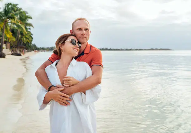 Photo of Couple in love hugging on the sandy exotic beach while they have a evening walk by the Trou-aux-Biches seashore on Mauritius island. People relationship and tropic honeymoon vacations concept image.