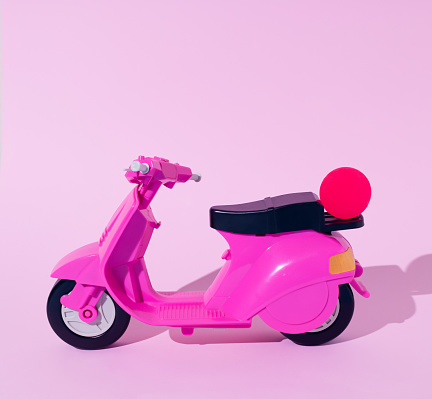 Pink moped toy with small ball isolated on a pastel pink background.