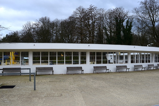 Diest, Flemish-Brabant, Belgium - January 15, 2023: free entrance open to public in Winter for a walk. Circular white wall with windows and  7 outdoor bench seats at the entrance area of the open air public swimming pool