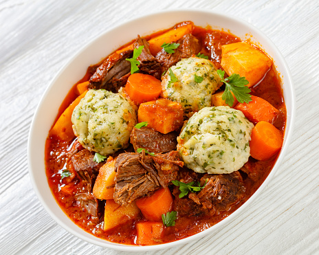 close-up of Beef Stew with Dumplings and vegetables in rich tomato and stock based gravy in white bowl, british cuisine, horizontal view from above
