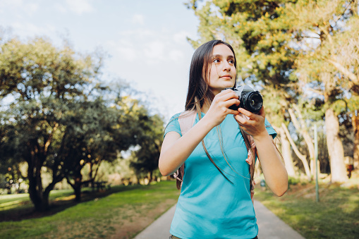 Beautiful young girl, taking photos with a vintage film camera outside in a public park