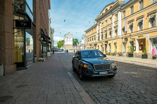 06-22-2022  Helsinki Finland. Luxury  car   (Bentley)  in downtown of Helsinki. Stores and old architecture in distance.