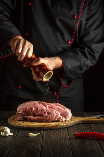 le chef prépare de la viande de veau crue. avant la cuisson, le chef ajoute du poivre au bœuf. le plat national est préparé dans la cuisine - veal calf meat baking photos et images de collection