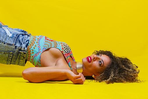 Portrait of a curly brunette Latina singer from Bogota Colombia between the ages of 40 and 44, in a studio against a yellow background wearing special clothing for the shoot