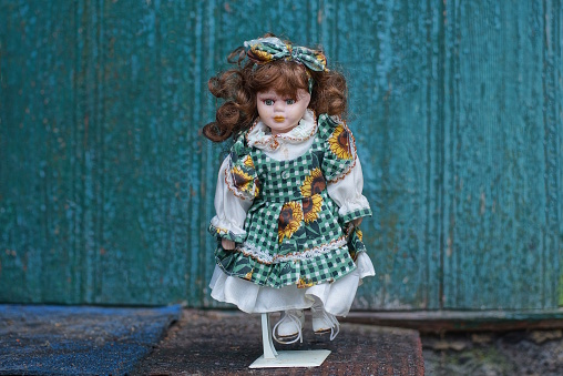 one plastic doll in a colored dress and brown hair stands on a gray table against a green wall
