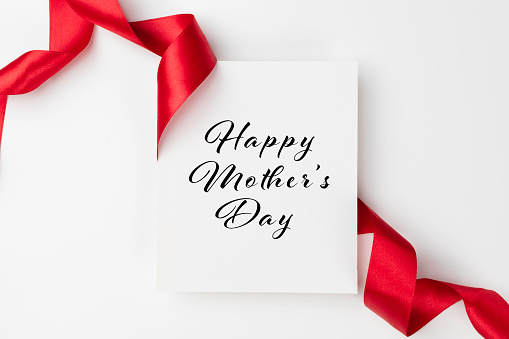 White greeting  card with Happy Mother’s day text on white background wrapped with a red colored ribbon.