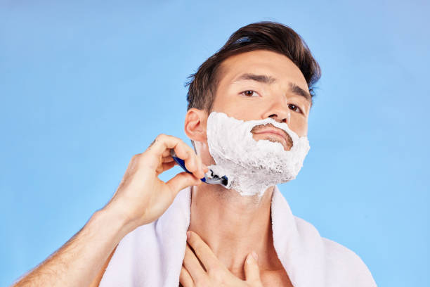 istock Portrait, shave and bathroom with a man model shaving his face in studio on a blue background for grooming. Beauty, skincare and shaving foam with a handsome young male using a razor in the morning 1456635801