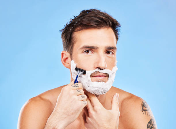 istock Portrait, shave and razor with a man model grooming in studio on a blue background for wellness or care. Face, skin and shaving with a handsome young male in the bathroom for facial hair removal 1456637314