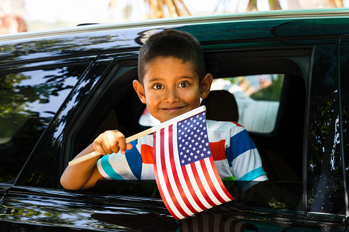 Little Boy in car is holding American flag with a cute smile.