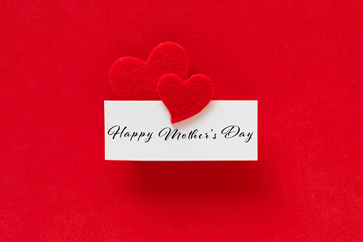 Red heart shapes attached to a white card with Happy Mother’s day text on red background.