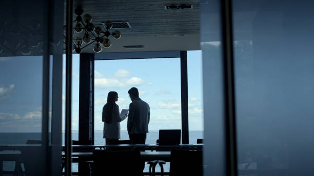 istock Two coworkers discussing business at panorama window. Managers silhouettes talk 1456639199