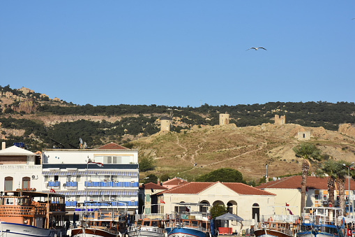 Foca, İzmir, Turkey 29 Jun 2021 The view of Foca with old windmills over the small harbor with daily tour boats parked in the harbor, hotels and \ncoffee shops