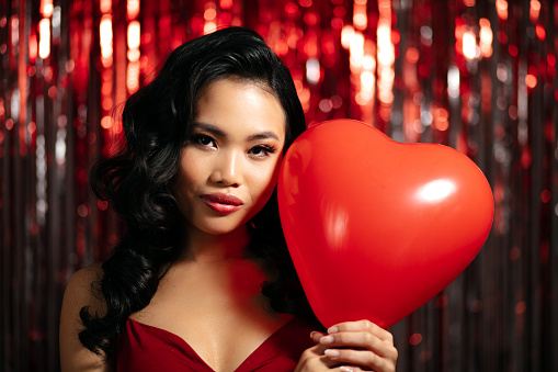 Young Beautiful Woman Posing With Heart-Shaped Balloon Over Shiny Red Background.