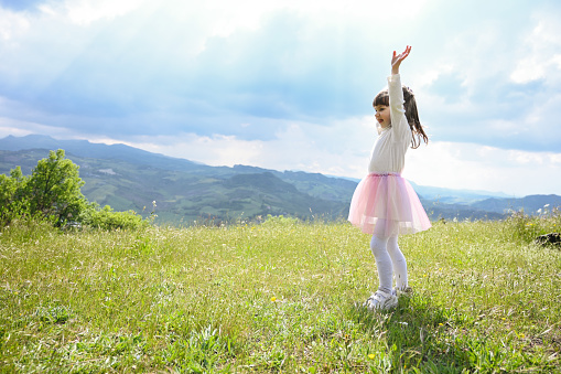 Summer, childhood, holidays, travel. little caucasian girl sitting on the meadow grass in a hill.