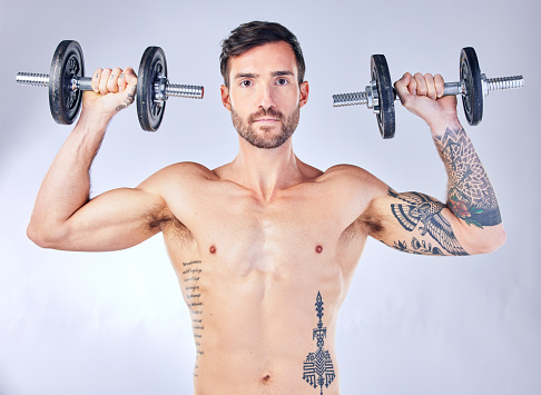 Portrait, exercise and man with weights for training, fitness and workout with grey studio background. Weightlifting, bodybuilder and healthy male with equipment for wellness, progress and body care.