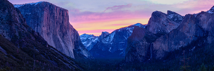 The sunrises over Yosemite Valley, the clouds illuminated pink while the granite walls begin to glow in the morning light of Yosemite National Park.
