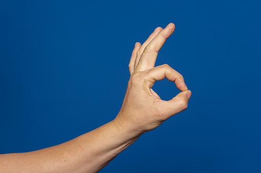 Strong hand of man making the ok gesture isolated on blue background. Everything ok, good job