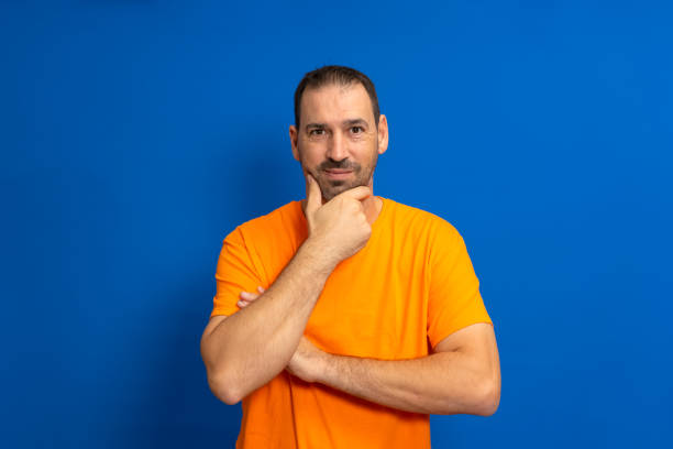 istock Curious handsome bearded latino man thinking with hand touching chin on isolated studio blue background. 1456644170