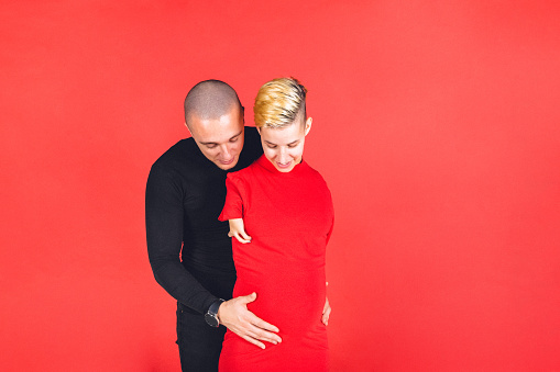 Young pregnant female adult with disability and her young male partner in studio portraiture.