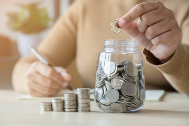 istock Woman with coins jar taking note to checklist expenses 1456658129