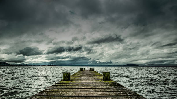 A wooden dock on the Superior lake surrounded by yellowing trees on a gloomy day in autumn in Michigan