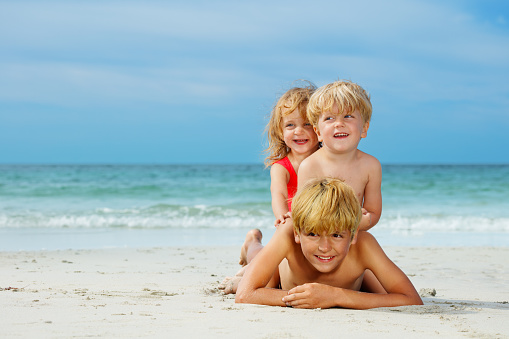 Group of three happy boys and a girl children lay on top of another on the sea sand beach at summer vacation