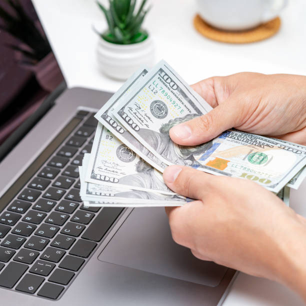 istock Male freelancer counting money or dollars in office while working on laptop. 1456659640