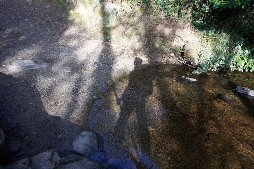 Shadow of an anonymous person with a stick and backpack crossing a river