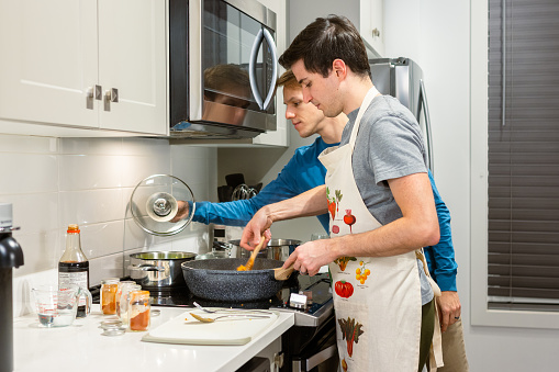 A young gay couple is cooking a vegan plant-based meal together in a modern kitchen.
