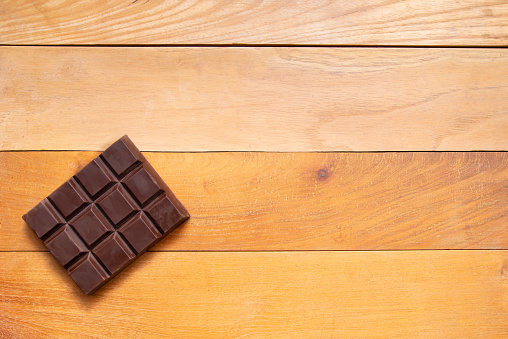 High angle view of dark chocolate tablet over rustic pine wood table.