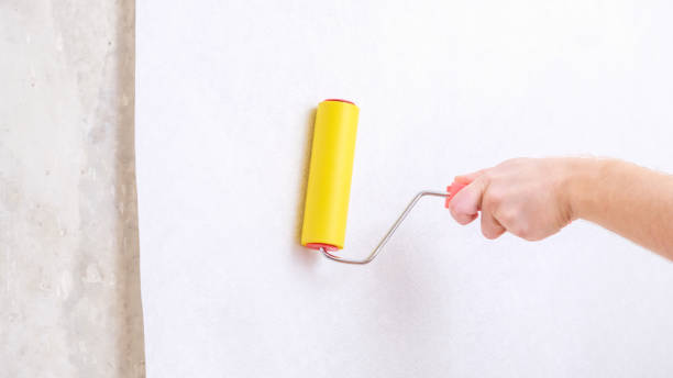 istock A man rolls out a canvas of white wallpaper with a suture wallpaper yellow roller. Removing air bubbles and glue from under the wallpaper. Wallpapering. 1456668470