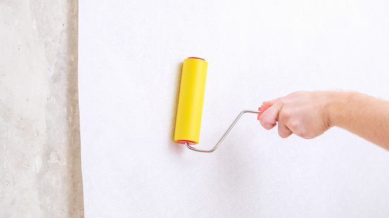 A man rolls out a canvas of white wallpaper with a suture wallpaper yellow roller. Removing air bubbles and glue from under the wallpaper. Wallpapering. Repair of a room, apartment, house.