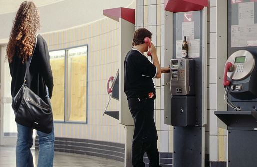 Cologne, Germany, July 11, 1999 - Young man making a phone call at a pay phone at Cologne Deutz station, a young lady waits until he is done