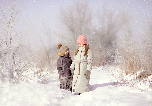 a boy and a girl of primary school age stand in a snowy park