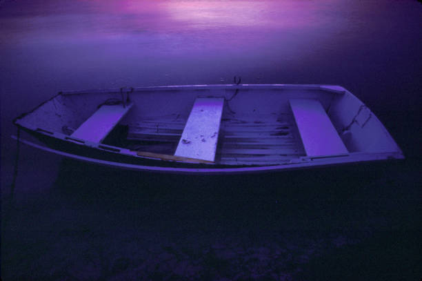 Wide shot of a 40-44-year-old Caucasian man sitting cross-legged meditating on a wooden jetty on a full lake of water overlooking mountains and woodlands with a moored rowboat with a dramatic purple orange coloured mood Cape Winelands South Africa