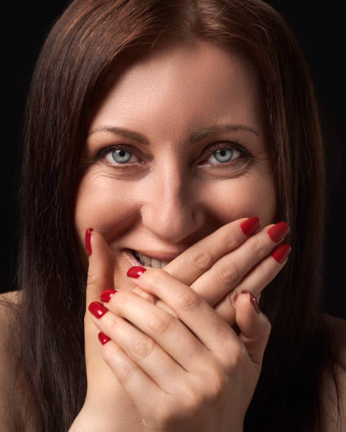 Cheerful woman laughing while covering mouth with her hands and gazing at camera. Studio portrait stock photo