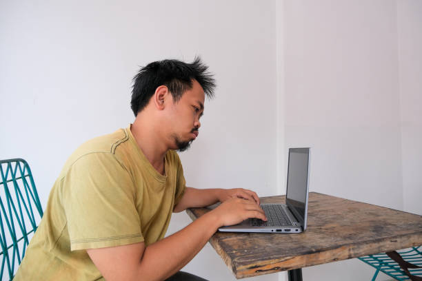 mężczyzna z azji południowo-wschodniej siedzący i pracujący przed laptopem z leniwym gestem - southeast asian ethnicity men laptop image type zdjęcia i obrazy z banku zdjęć