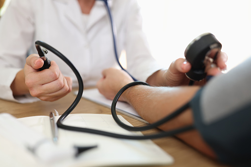Close-up of doctors hand measuring blood pressure of male patient. Clinic or hospital office. Medicine and health care concept