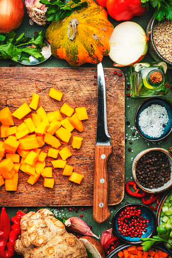 Food background. Sliced pumpkin and knife on cutting board. Vegetables, mushrooms, roots, spices - ingredients for vegan, cooking. Healthy eating, diet, comfort slow food. concept. Rustic table, top view