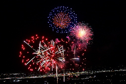 Summer festival or celebration, vibrant colors exploding fireworks against night sky above city lights.