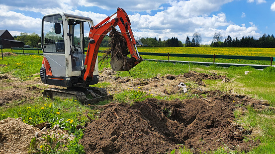 Work on the construction site of a house. The excavator digs out roots. A small digger in the garden