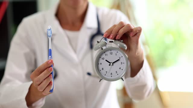 Doctor dentist showing alarm clock and toothbrush in clinic closeup 4k movie slow motion