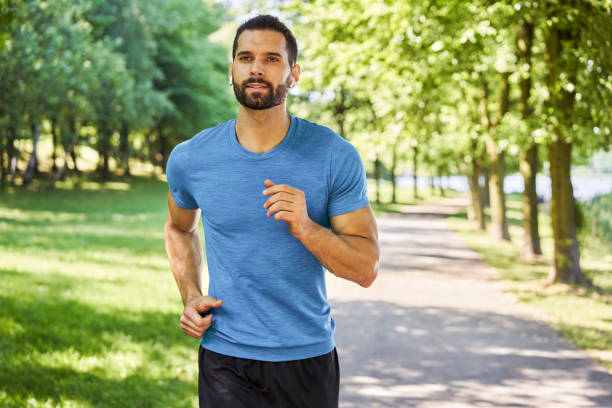 Active young man running with earphones in park during sunny day in spring summer stock photo