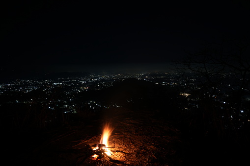 Bonfire on a mountain top during the winter at night overlooking a city.